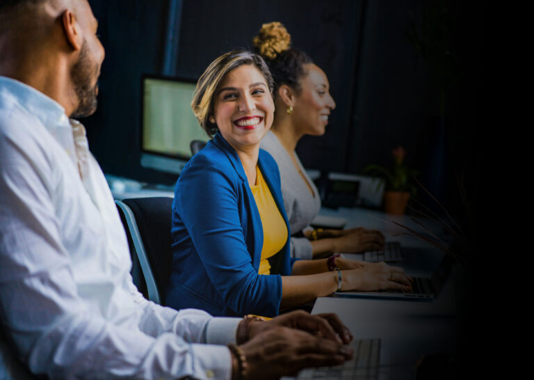 "Employee Engagement for Health Insurers: A diverse team of professionals collaboratively working with a sense of camaraderie, highlighted by a woman in a blue blazer smiling engagingly at a colleague."
