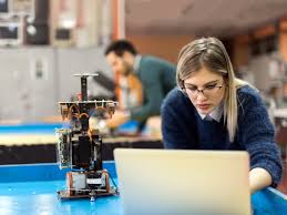 The student is using a laptop, and there’s a robotic or tech prototype on the table, suggesting hands-on work with advanced technology. Another person is in the background, indicating a collaborative space. This image is a perfect fit for your webpage on "Build startup with AI advancement in GTA" at Sheridan College, and here’s why it should be included: